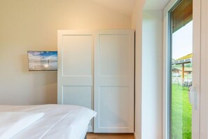 A bedroom with a bed, a TV mounted on the wall, and a sliding glass door leading to a balcony. - Ferienhaus mit eigener Sauna und grossem Garten (Tönning OT Kating)