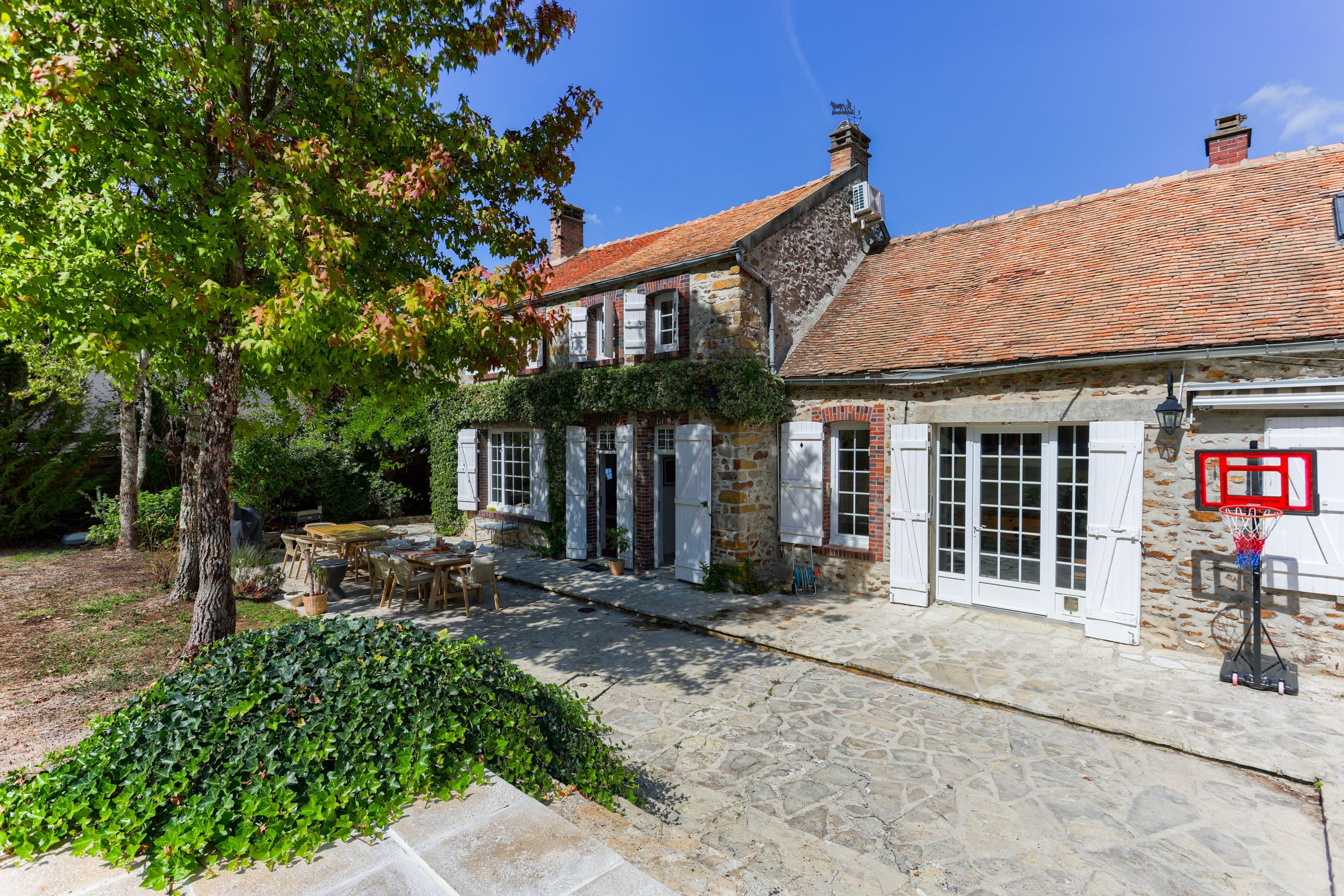A traditional stone building with a tiled roof, a covered outdoor seating area, and a basketball hoop.