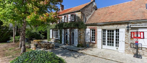A traditional stone building with a tiled roof, a covered outdoor seating area, and a basketball hoop.