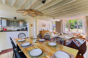 A dining area with a wooden table set for six, surrounded by chairs, and a kitchen in the background. - La Prairie Authenticité et Confort -piscine privée (Villeneuve-les-Bordes)