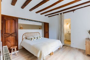 A bedroom with a wooden bed, a wooden bench, a small stool, and a bathroom visible through an open door. - La Prairie Authenticité et Confort -piscine privée (Villeneuve-les-Bordes)