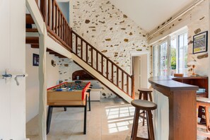 A room with a foosball table, a wooden staircase, and a bar area. - La Prairie Authenticité et Confort -piscine privée (Villeneuve-les-Bordes)