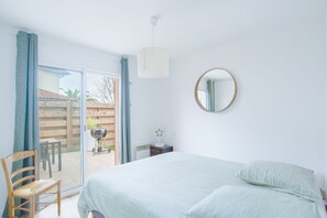 Un dormitorio con cama, una silla, una mesita con un ventilador y una puerta corrediza de vidrio que da a un área exterior.