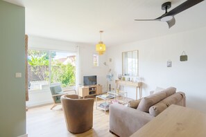 Ein modernes Wohnzimmer mit einer Couch, einem Sessel, einem Couchtisch, einem Fernseher und einem Deckenventilator.