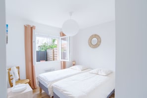 Un dormitorio con dos camas, una ventana con cortinas, una lámpara de noche y un adorno en la pared.