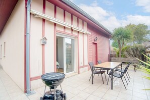 Eine Terrasse mit Grill, Tisch, Stühlen und einer Glasglastür, die zu einem Innenraum führt.