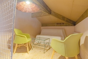 Ein kleiner, gemütlicher Raum mit einem Bett, zwei grünen Sesseln, einem Glastisch und einer gewobenen Lampe.
