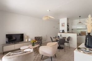 Ein modernes Wohnzimmer mit Flachbildfernseher, Essbereich mit Tisch und Stühlen, Küche mit weißen Schränken und Deckenventilator.