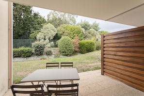 Eine Terrasse im Freien mit Tisch und Stühlen, umgeben von einem Holzzaun und verschiedenen Sträuchern.