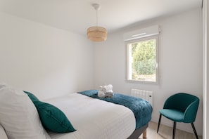 A bedroom with a bed, a chair, a window, and a radiator. - Pic épeiche - proche de la plage (Pléneuf-Val-André)