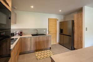 A modern kitchen with a built-in oven, a stainless steel refrigerator, and a wooden door. - Chalet Soline La Glière - Appartement avec jardin (Samoëns)