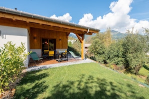 A wooden house with a covered patio, outdoor furniture, and a view of the surrounding landscape. - Chalet Soline La Glière - Appartement avec jardin (Samoëns)