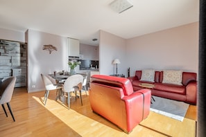A modern living room with a red leather sofa, a dining area with a table and chairs, and a kitchen in the background. - L'échappée Vannetaise - T2 avec parking privé (Vannes)
