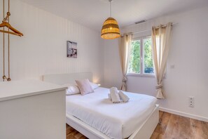 Un dormitorio con cama, lámpara colgante, ventana con cortinas e imagen colgada en la pared.