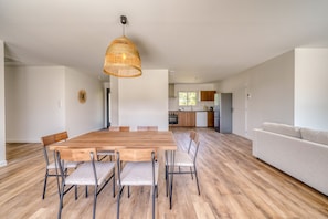 A modern interior with a dining area featuring a wooden table and chairs, a kitchen with wooden cabinets, and a living area with a sofa. - La Casa Romarin - Proche Libourne (Galgon)
