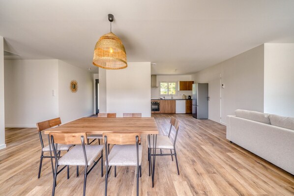 Un interior moderno con comedor que incluye mesa y sillas de madera, cocina con armarios de madera y sala de estar con sofá.