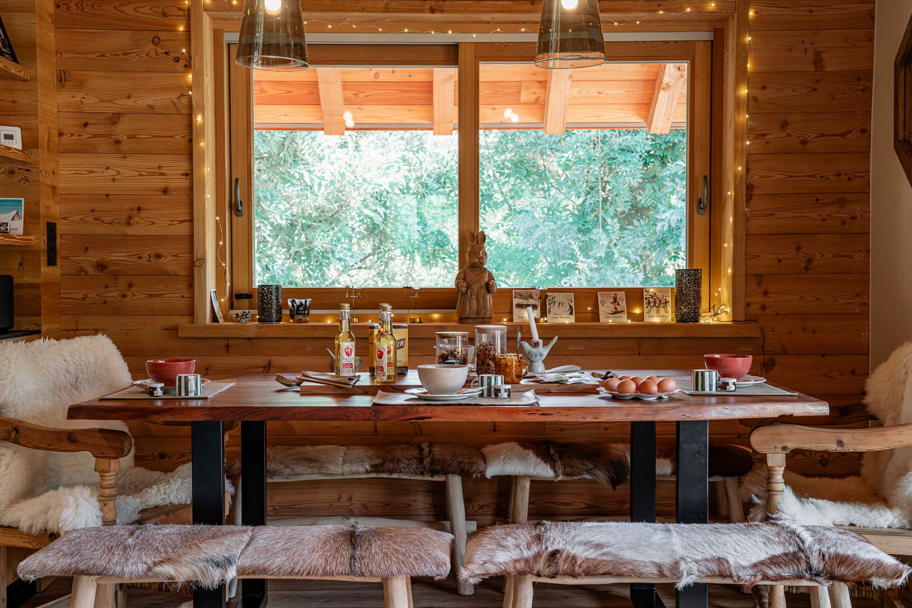 A wooden interior with a large window, wooden benches, and a table with various items.