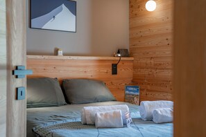 A bedroom with a wooden headboard, a bed with grey bedding, two pillows, a small shelf with a lamp, and a framed picture on the wall. - Chalet Casacamo - Chalet au pied des pistes (La Salle-les-Alpes)
