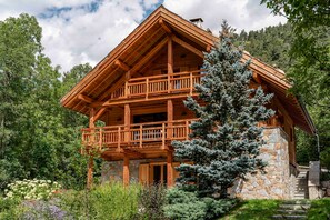 A two-story log cabin with a balcony, surrounded by lush greenery and a stone foundation. - Chalet Casacamo - Chalet au pied des pistes (La Salle-les-Alpes)