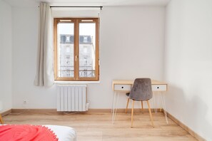 Een kamer met een houten bureau, een grijze stoel, een radiator en een raam met gordijnen.