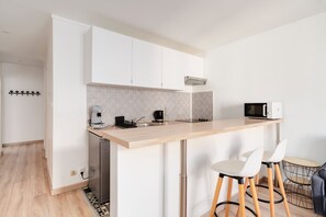 A modern kitchen with a wooden countertop, a built-in microwave, a coffee machine, and a sink. There are two white bar stools and a small round table with chairs. - Le Mozart nancéen - proche du centre-ville (Nancy)