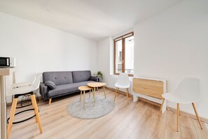 Ein modernes Wohnzimmer mit einem grauen Sofa, einem kleinen runden Tisch, einem weißen Sessel und einer Heizung.