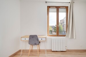 A room with a wooden desk, a grey chair, a radiator, and a window with a view of buildings. - Le Mozart nancéen - proche du centre-ville (Nancy)