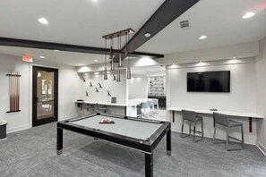 Ein Billardtisch mit Billardzubehör, eine Bar mit Hockern und ein an der Wand befestigter Fernseher.