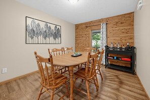 A dining area with a wooden table and chairs, a wall-mounted artwork, and a built-in wooden cabinet with bottles. - Lake Cumberland Views, Hot Tub & Room for 11 (Somerset)
