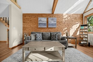 A modern living room with a wooden floor, a grey sofa with patterned cushions, a wooden coffee table with drawers, and a wooden wall with two framed pictures. - Lake Cumberland Views, Hot Tub & Room for 11 (Somerset)