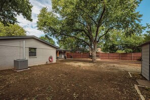 A backyard with a covered patio, a tree, and a fenced area. - Modern 3BR Oasis with Hot Tub and Pool Table (Abilene)