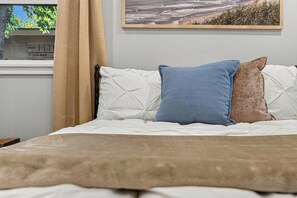 A bed with white bedding and three pillows in different colors. - Modern 3BR Oasis with Hot Tub and Pool Table (Abilene)