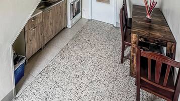 A compact kitchen with a gas stove, wooden cabinets, a dining table with chairs, and a speckled floor.