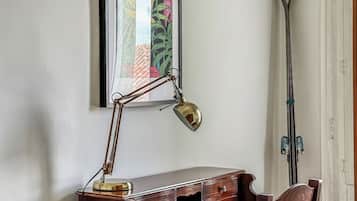 A wooden desk with a desk lamp, a chair, and a framed picture on the wall.