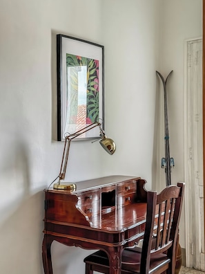A wooden desk with a desk lamp, a chair, and a framed picture on the wall.