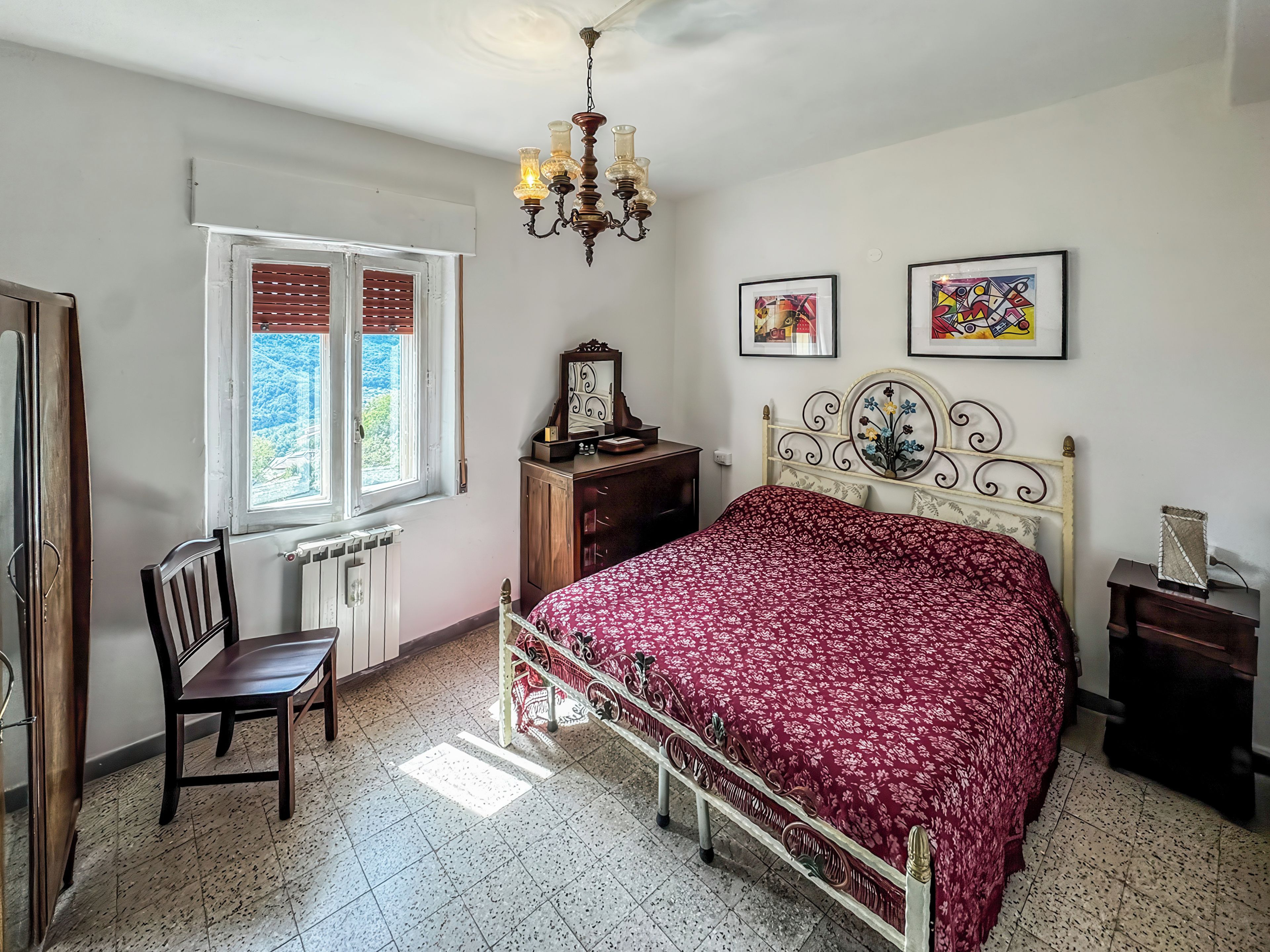 Un dormitorio con cama, escritorio, silla, cómoda y ventana con contraventanas.