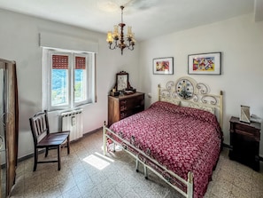 A bedroom with a bed, a desk, a chair, a dresser, and a window with shutters.