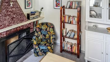 Ein Wohnzimmer mit Kamin, Bücherregal, gemustertem Sessel und Schrank.