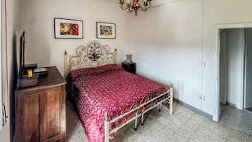 Ein Schlafzimmer mit Bett, Schminktisch, einer Kandelaber und zwei gerahmten Kunstwerken an der Wand.