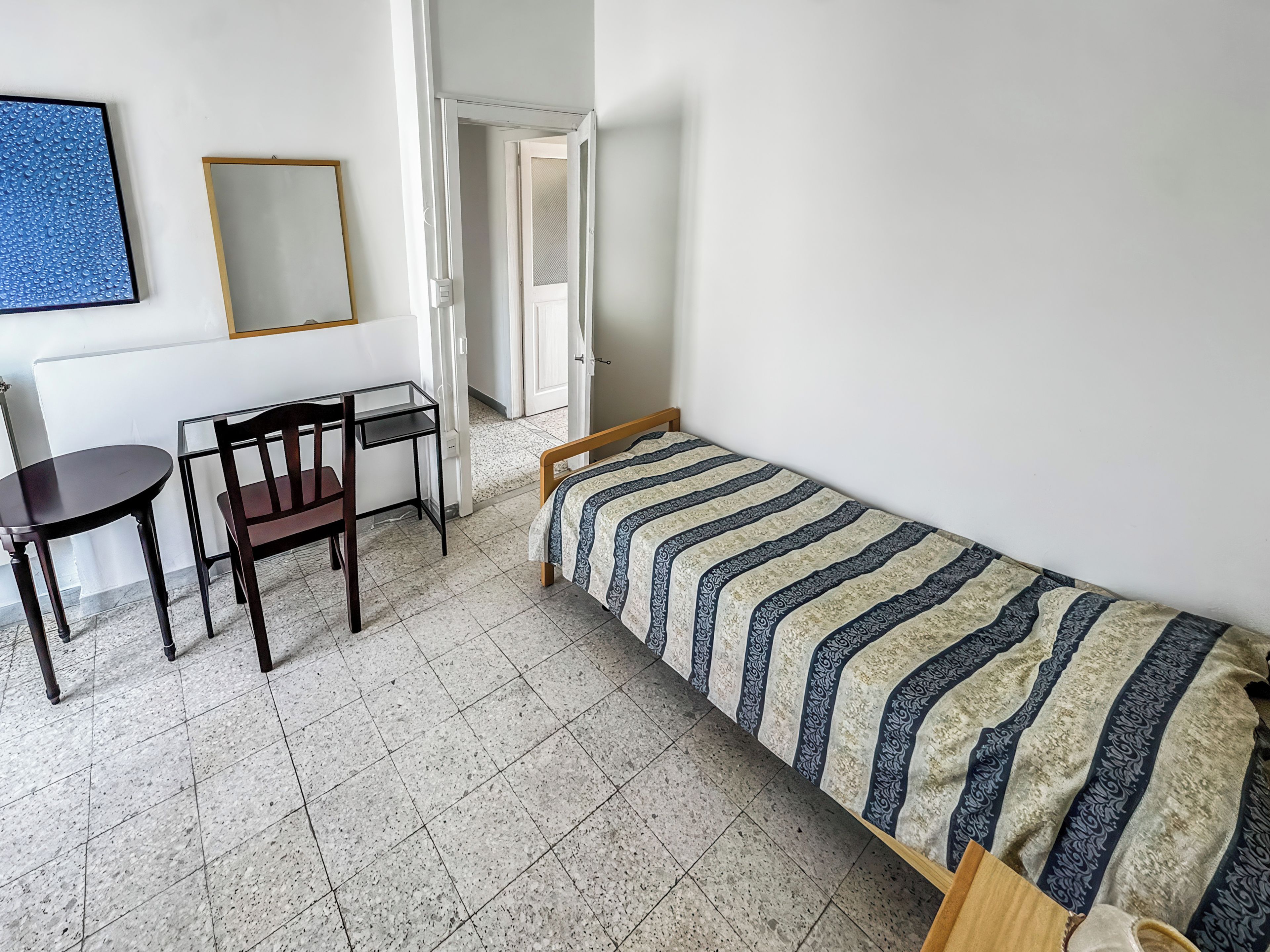 A small, sparsely furnished room with a bed, a table, and a chair.