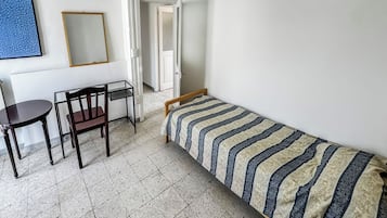 A small, sparsely furnished room with a bed, a table, and a chair.
