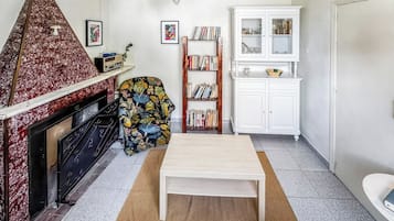 A living room with a fireplace, a bookshelf, a coffee table, and a patterned armchair.