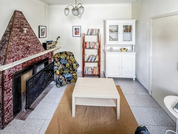A living room with a fireplace, a bookshelf, a coffee table, and a patterned armchair.