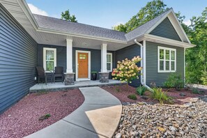 A residential house with a front porch, a stone fireplace, and a garden with a variety of plants. - Pet Friendly-Baileys Harbor Home with Fire Pit (Baileys Harbor)
