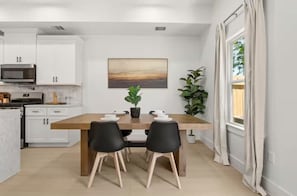A modern kitchen with white cabinets, a microwave, and a dining area with a wooden table and black chairs. - “Luxury Living Meets Comfort – 4BR Dream Stay” (Houston)