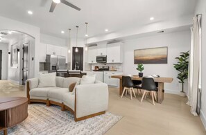 Una sala de estar moderna con un sofá, un comedor con mesa y sillas, y una cocina al fondo.
