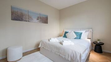 Een slaapkamer met een bed, nachtkastje, een klein rond tafeltje en een witte vloerkleed.