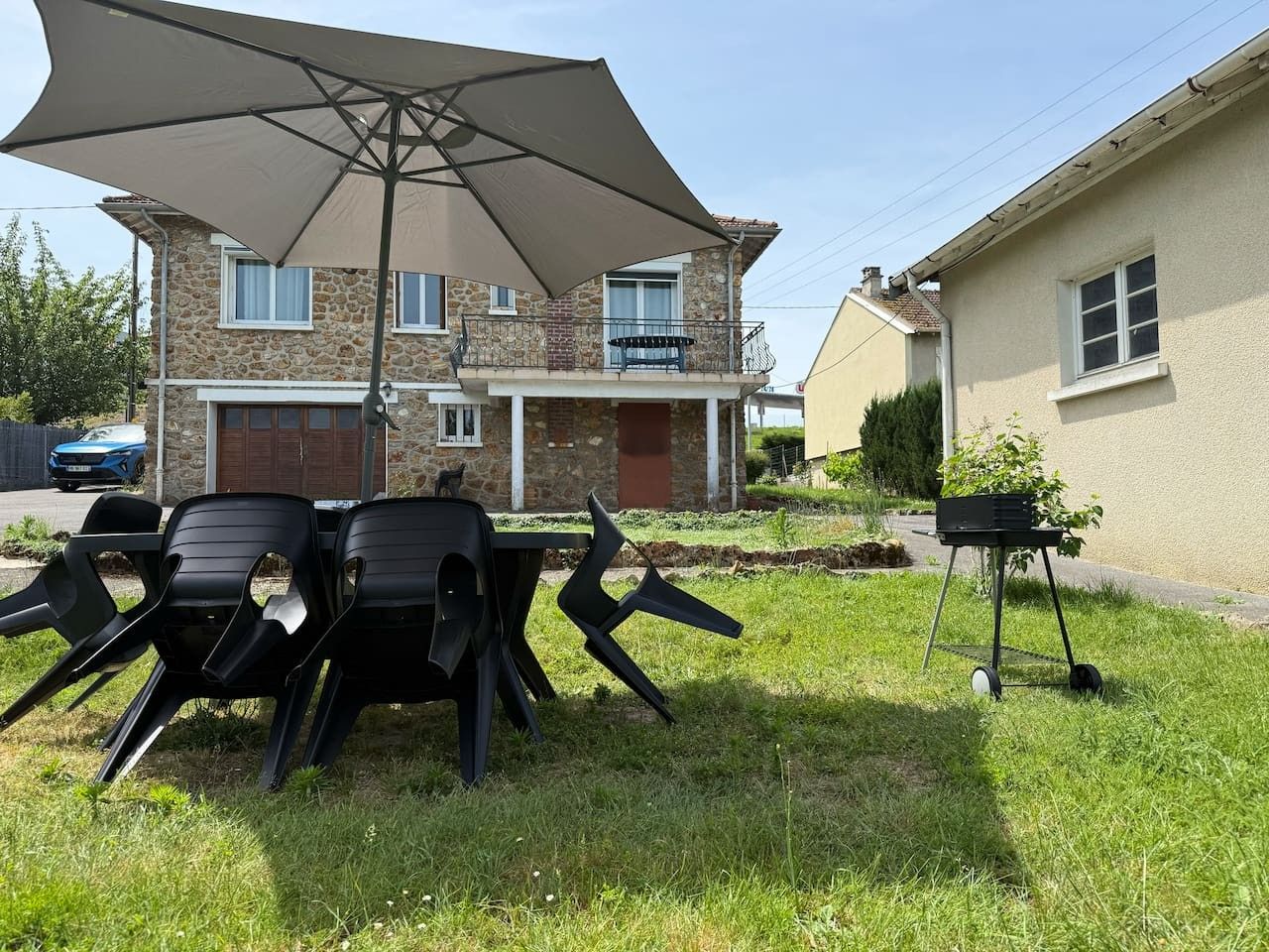 Buiten zitplaatsen met een tafel, stoelen, een grote parasol en een barbecue.