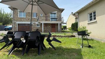 Buiten zitplaatsen met een tafel, stoelen, een grote parasol en een barbecue.
