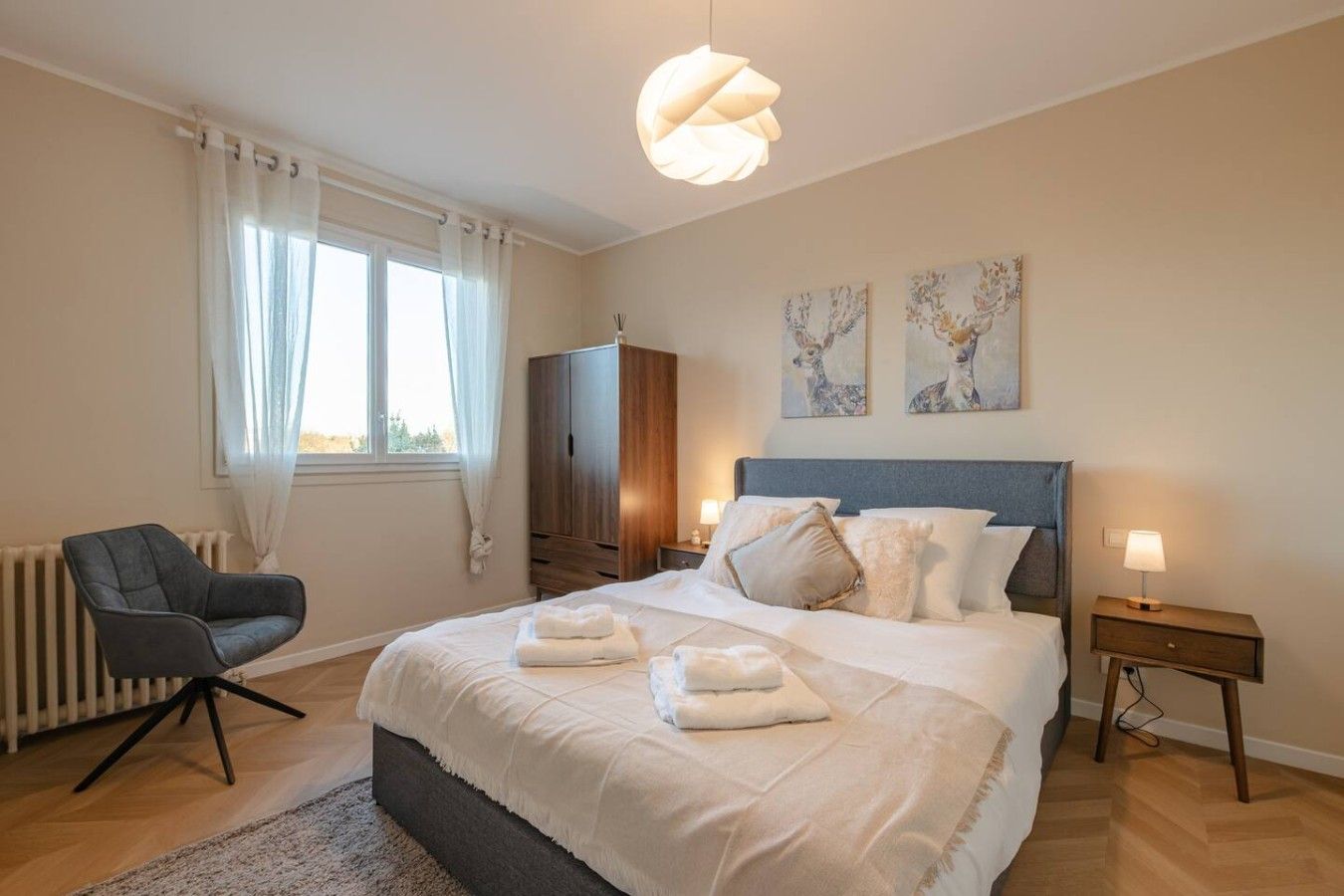 Ein Schlafzimmer mit Bett, Nachttischen, einem Sessel, einem Kleiderschrank und Bildern an der Wand.